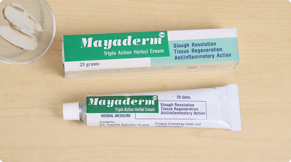 Mayaderm Triple Action Herbal Cream 25g tube and packaging box placed on a light wood surface.