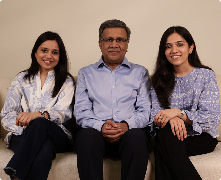 A family portrait of a man and two women sitting together on a light-colored sofa against a plain beige wall. 